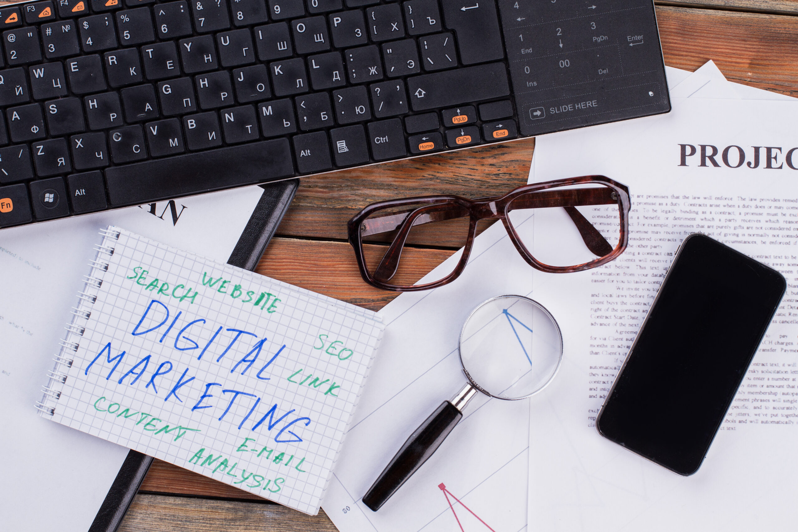 Digital marketing on notepad and various business papers on brown background. Digital marketing on notepad and various business papers on brown background. Brown glasses magnifier and smartphone near notepad.